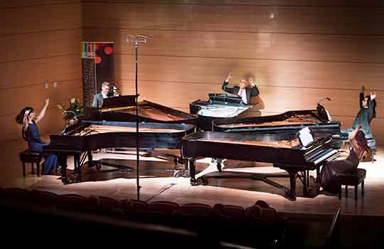 Four players playing piano on stage.