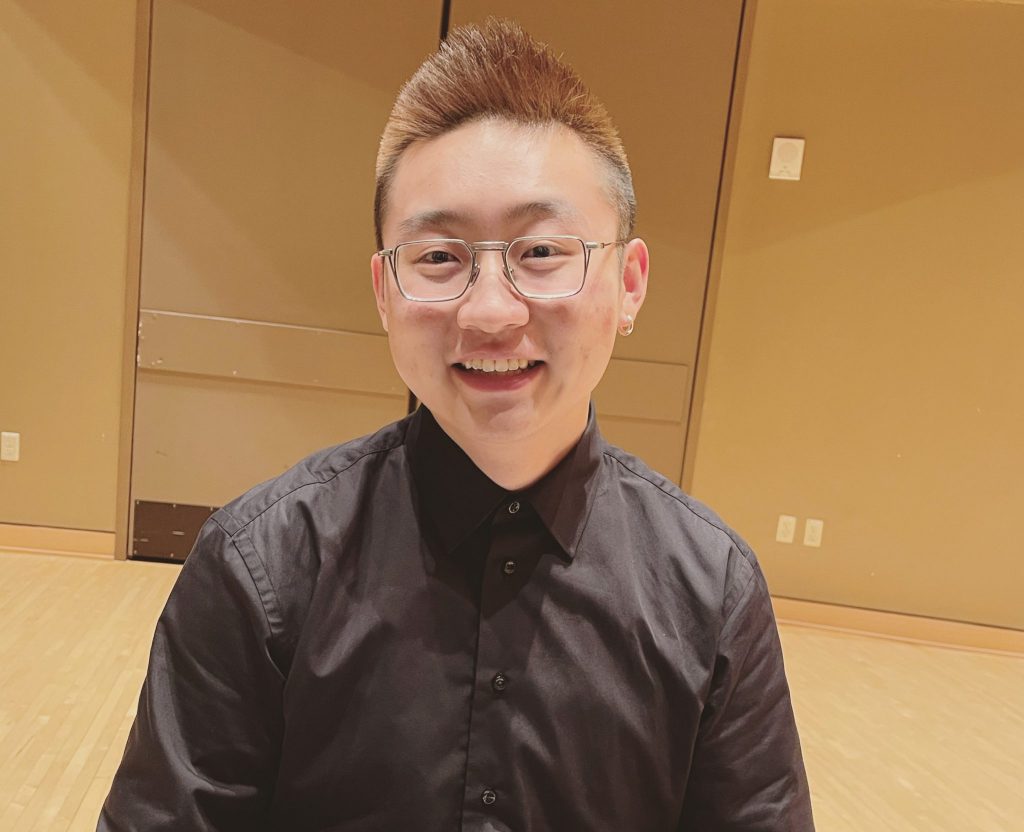 Boran Zhao smiling at the camera as he sits at the keyboard of a piano.